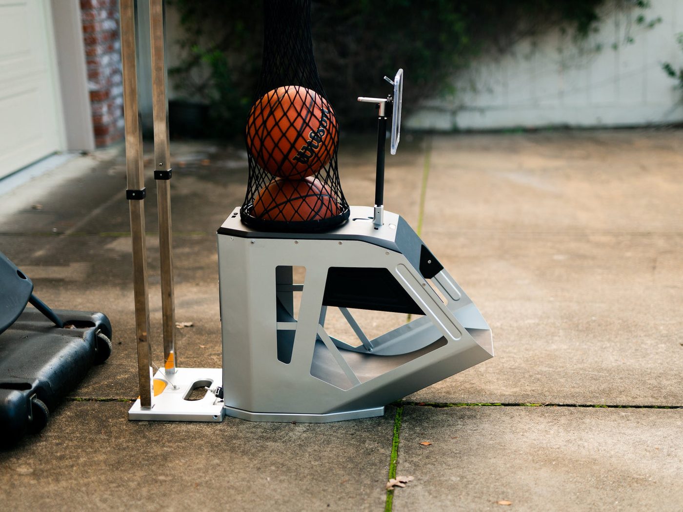 The Hoopfit machine on a driveway under a basketball hoop, holding a ball