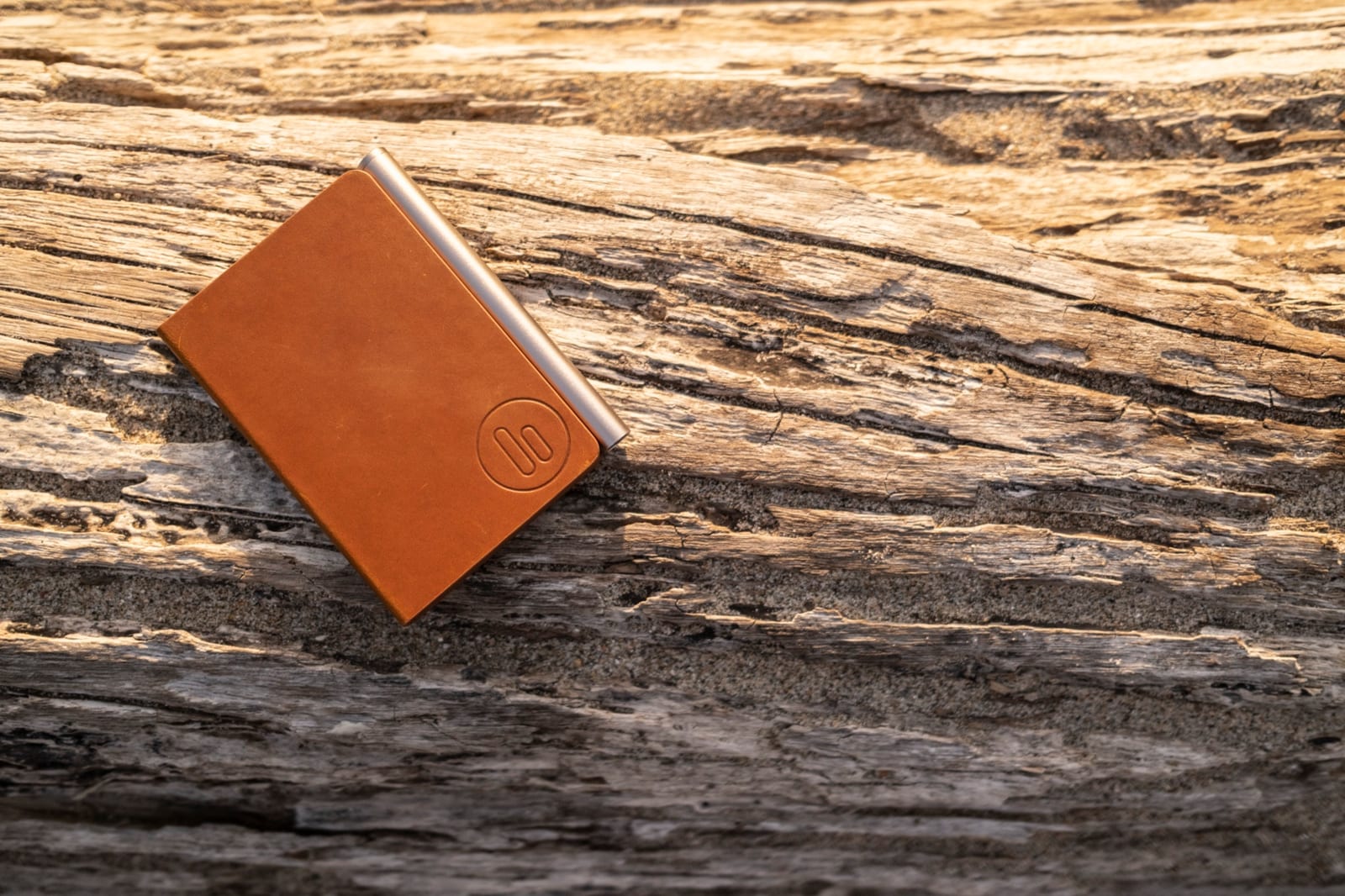 A closed brown leather noble. note on weathered wood, with the machined aluminium spine catching the light