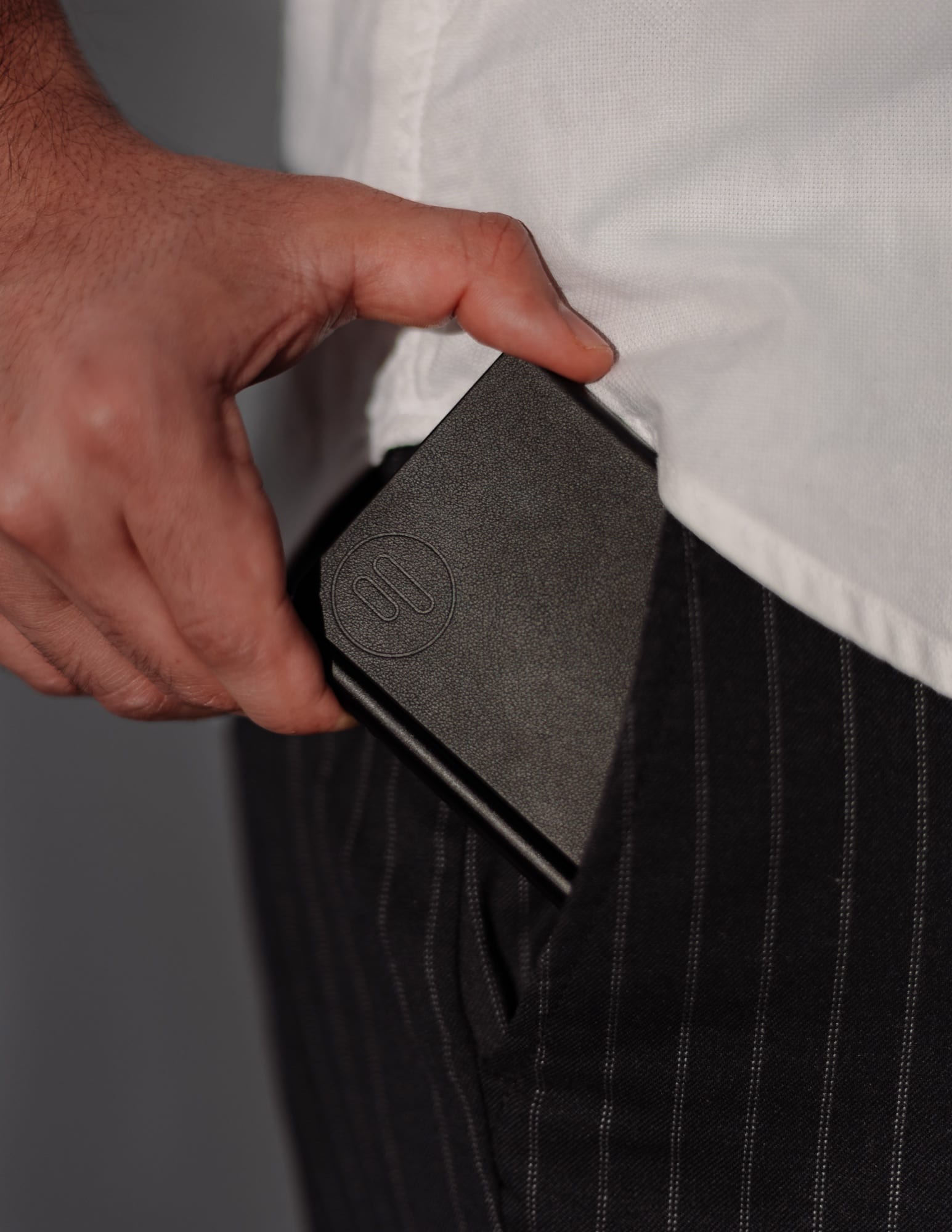 A hand sliding the black noble. note into a trouser pocket
